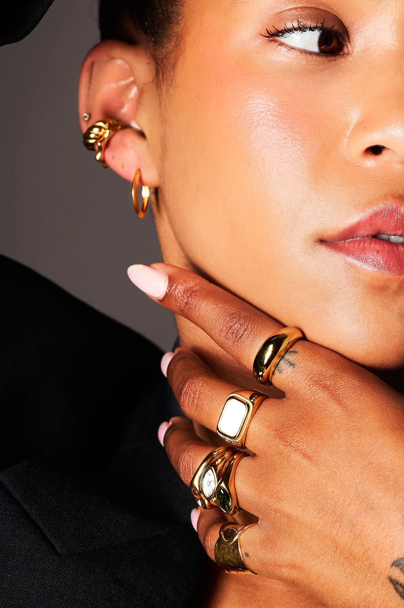 Woman wearing gold statement rings and gold hoop earrings, close-up fashion jewelry