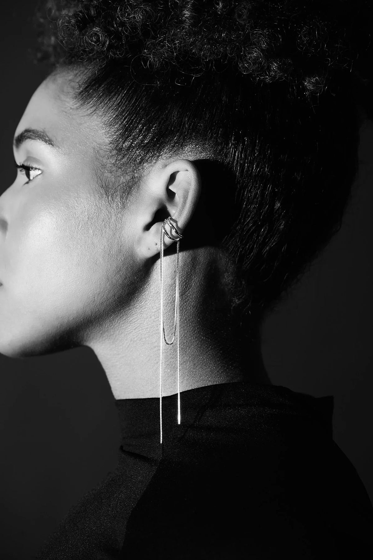 Woman wearing modern long silver chain earring with ear cuff, close-up profile