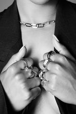 Woman wearing chunky silver rings and a bold chain necklace in black blazer