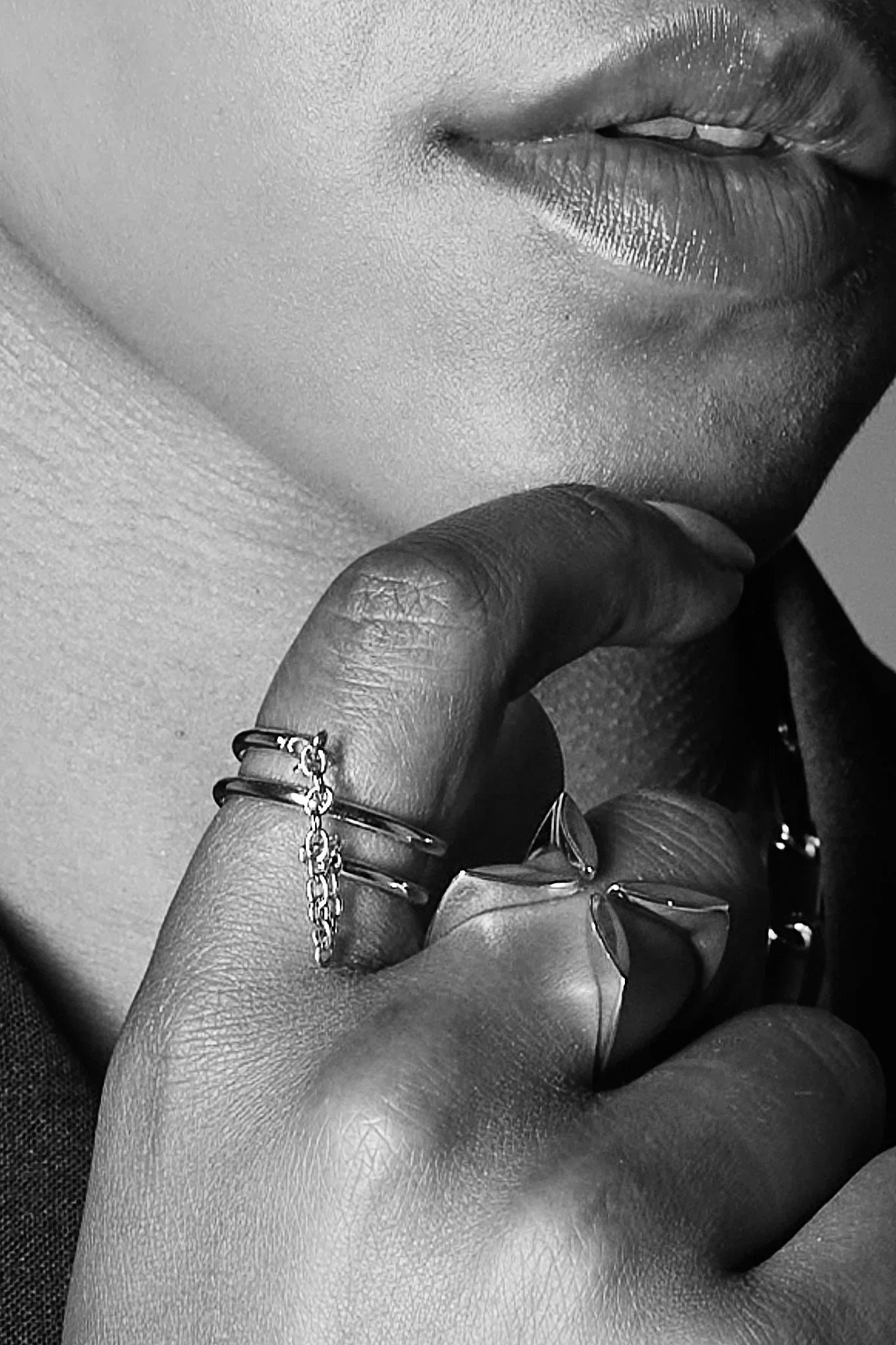 Close-up of a hand wearing modern silver rings, one with a chain detail, near lips.
