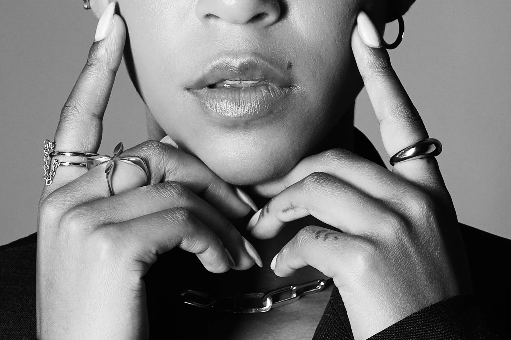 Close-up of woman wearing modern silver rings, a chunky chain necklace, and hoop earring