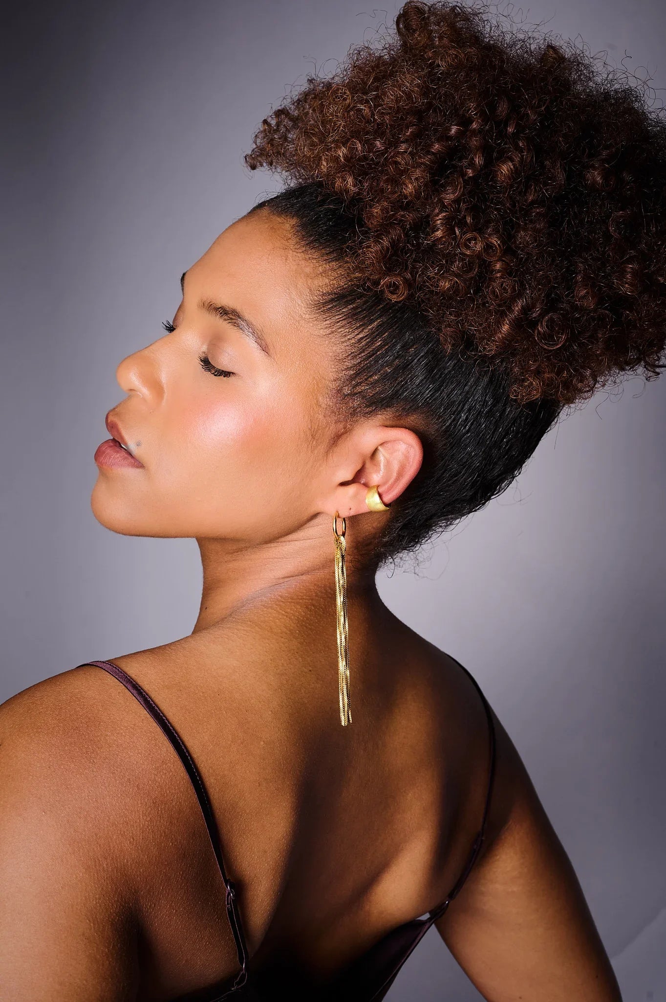 Woman wearing long gold statement earring, elegant studio jewelry portrait