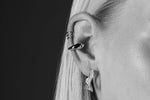 Close-up of a woman's ear with modern silver earrings and ear cuffs, minimalist jewelry
