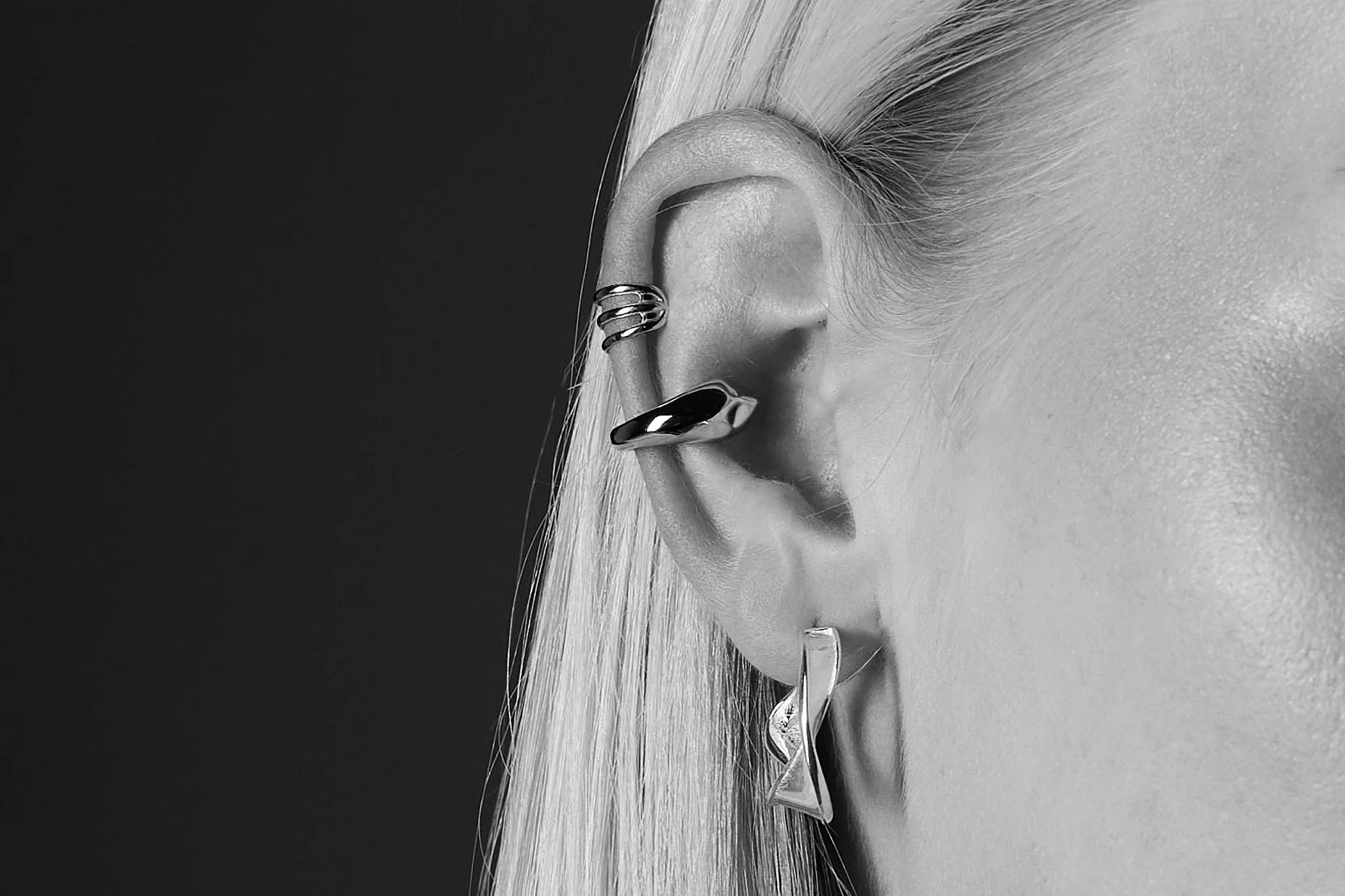 Close-up of a woman's ear with modern silver earrings and ear cuffs, minimalist jewelry