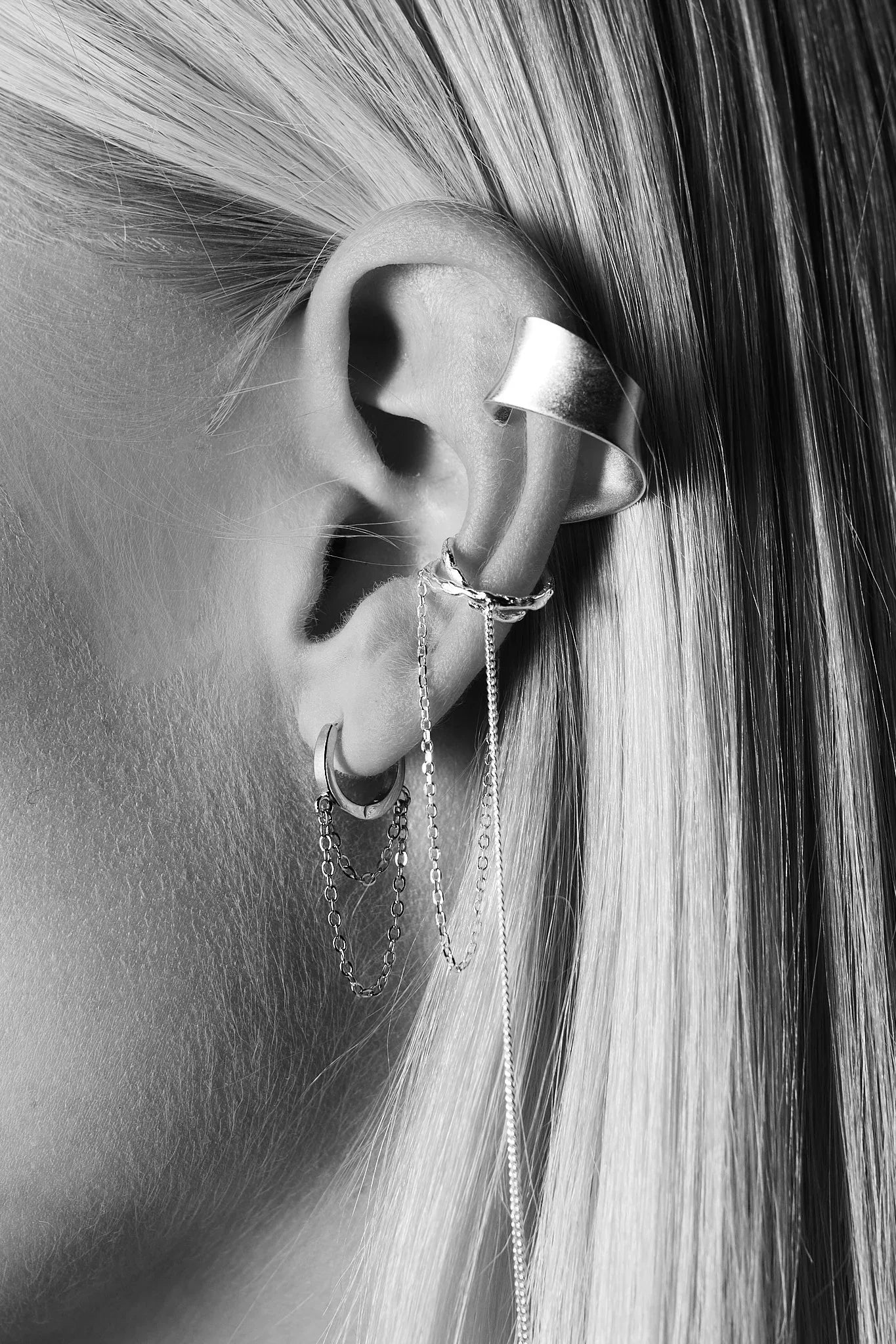 Close-up of ear with layered silver ear cuffs, hoop earrings, and chain jewelry