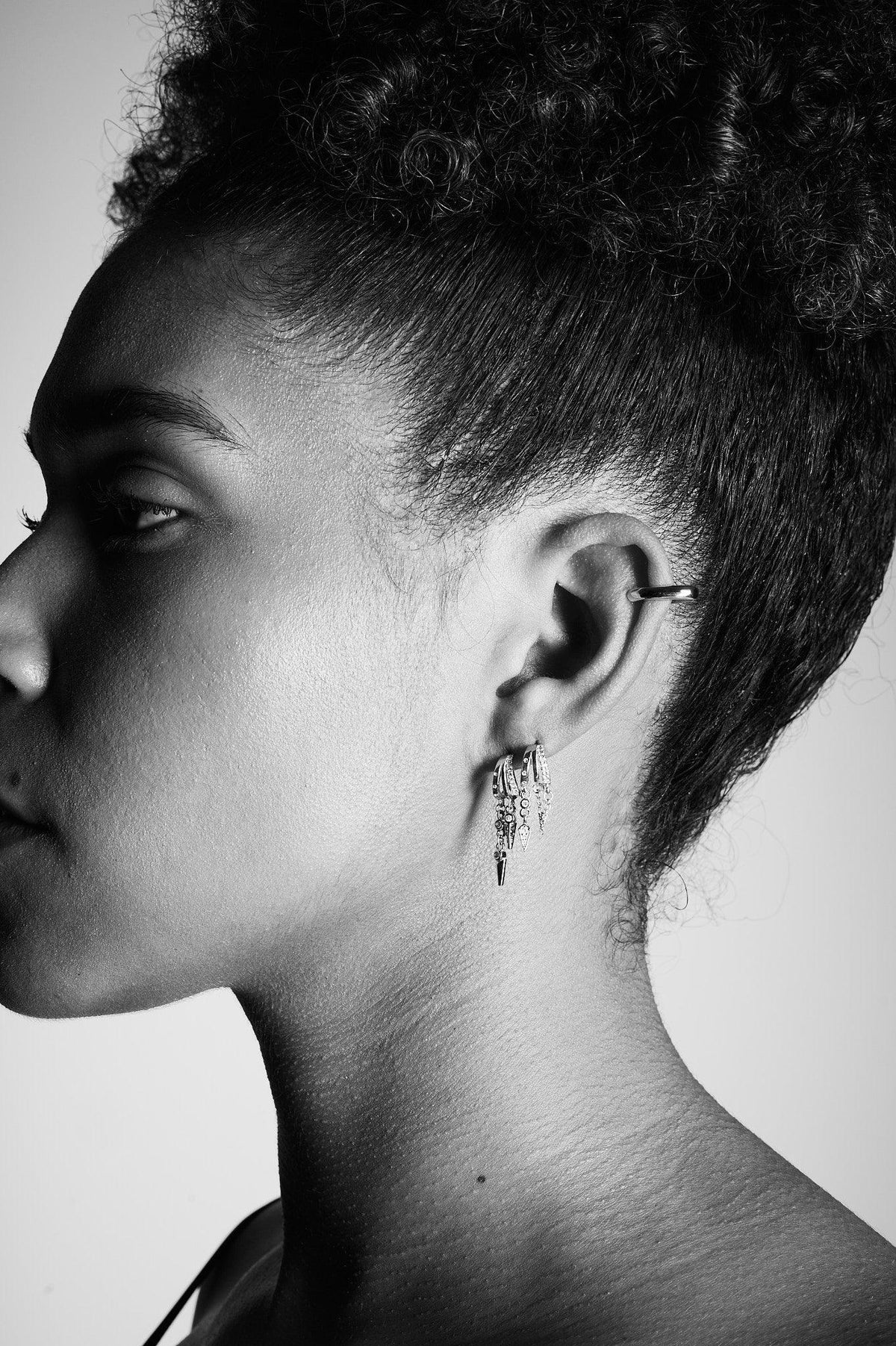 Close-up side profile of a woman wearing layered silver dangle earrings and ear cuff