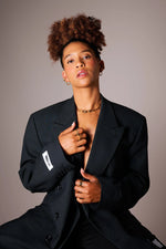 Stylish woman wearing gold necklaces, rings, and hoop earrings in a black blazer