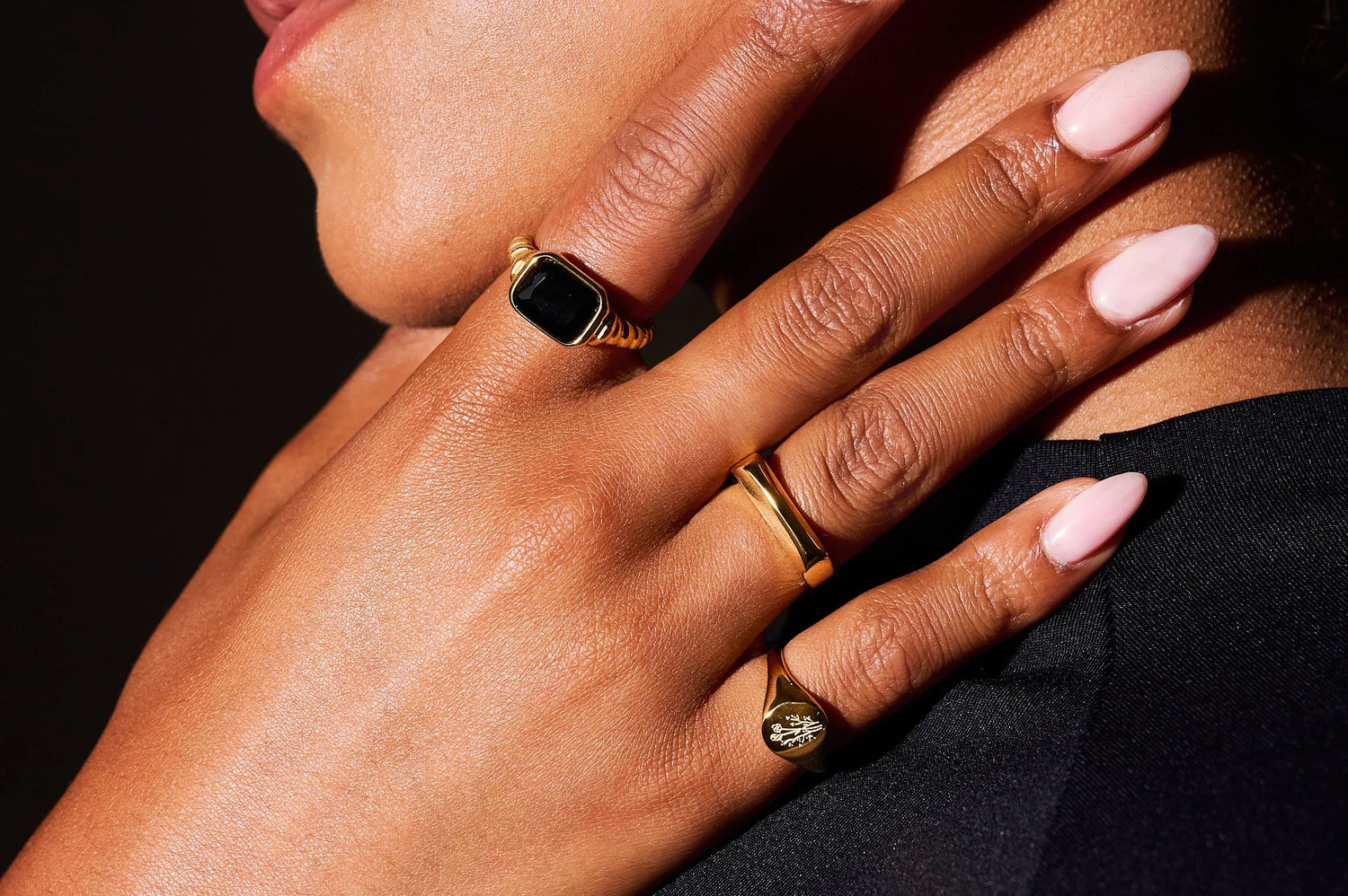 Close-up of a hand with manicured nails wearing three gold rings, one with a black stone
