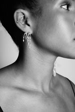 Close-up of woman wearing multiple silver dangle hoop earrings, minimalist jewelry style