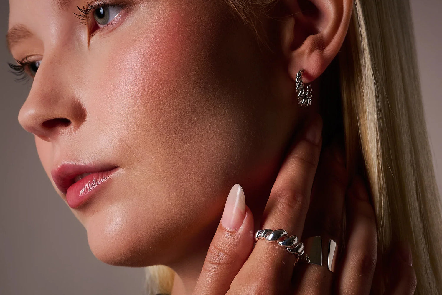 Woman wearing silver twisted hoop earring and chunky silver rings, close-up jewelry shot