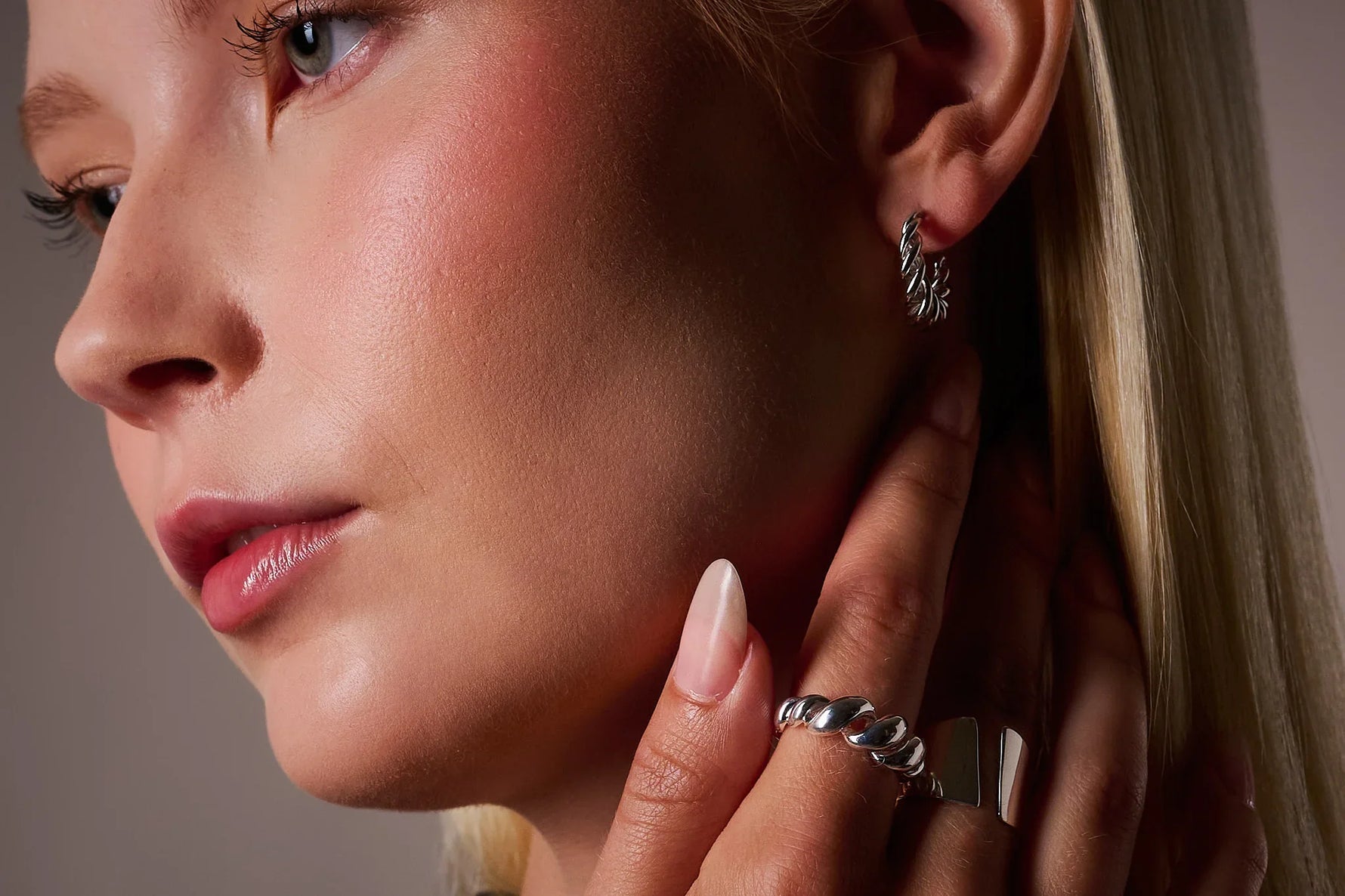 Woman wearing silver twisted hoop earring and chunky silver rings, close-up jewelry shot