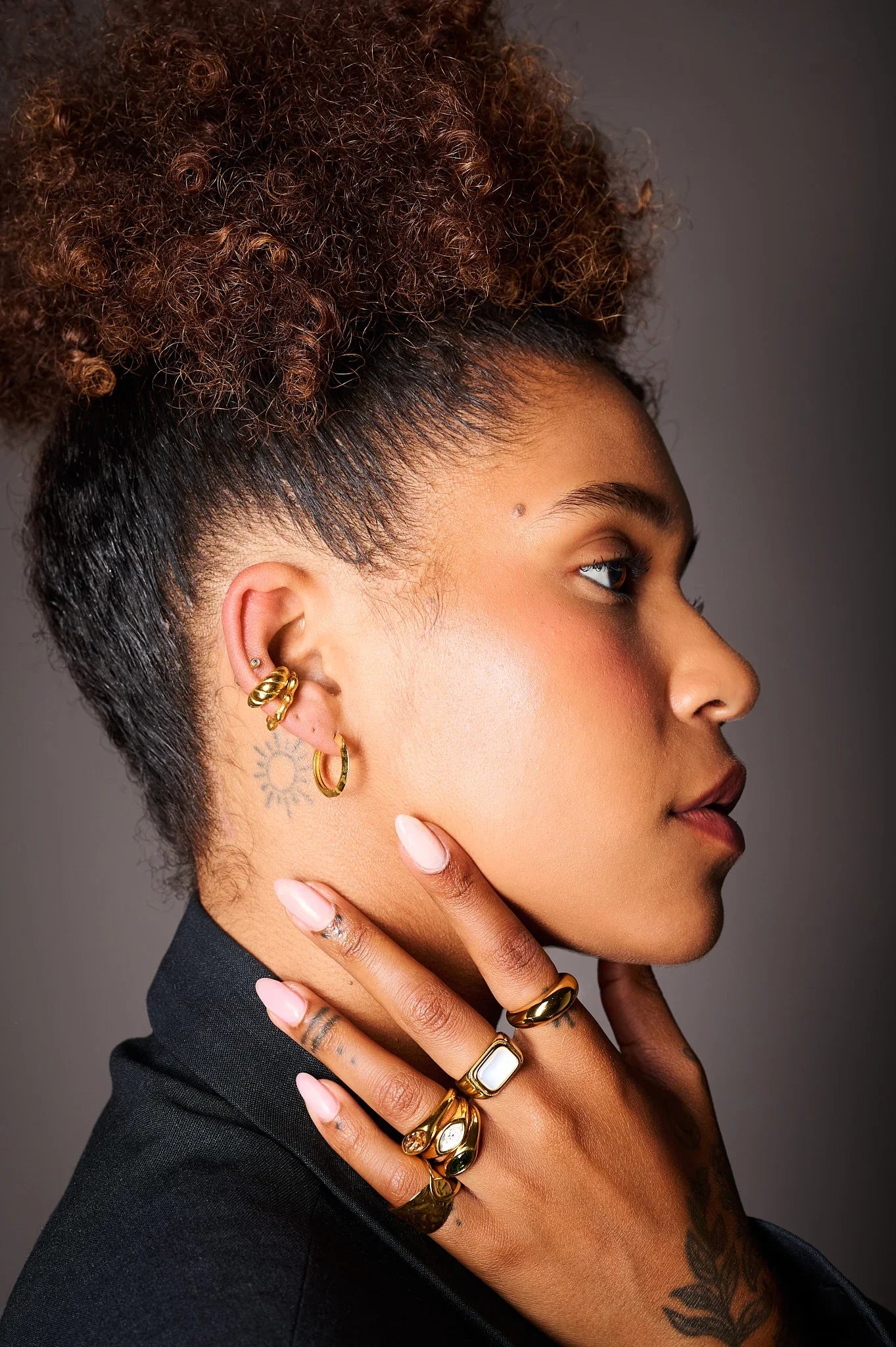 Woman wearing multiple gold rings and hoop earrings, close-up jewelry fashion shot