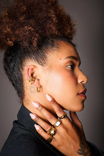 Woman wearing gold hoop earrings and chunky gold rings, close-up jewelry photo