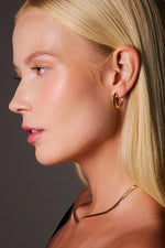 Woman wearing gold hoop earring and sleek gold snake chain necklace