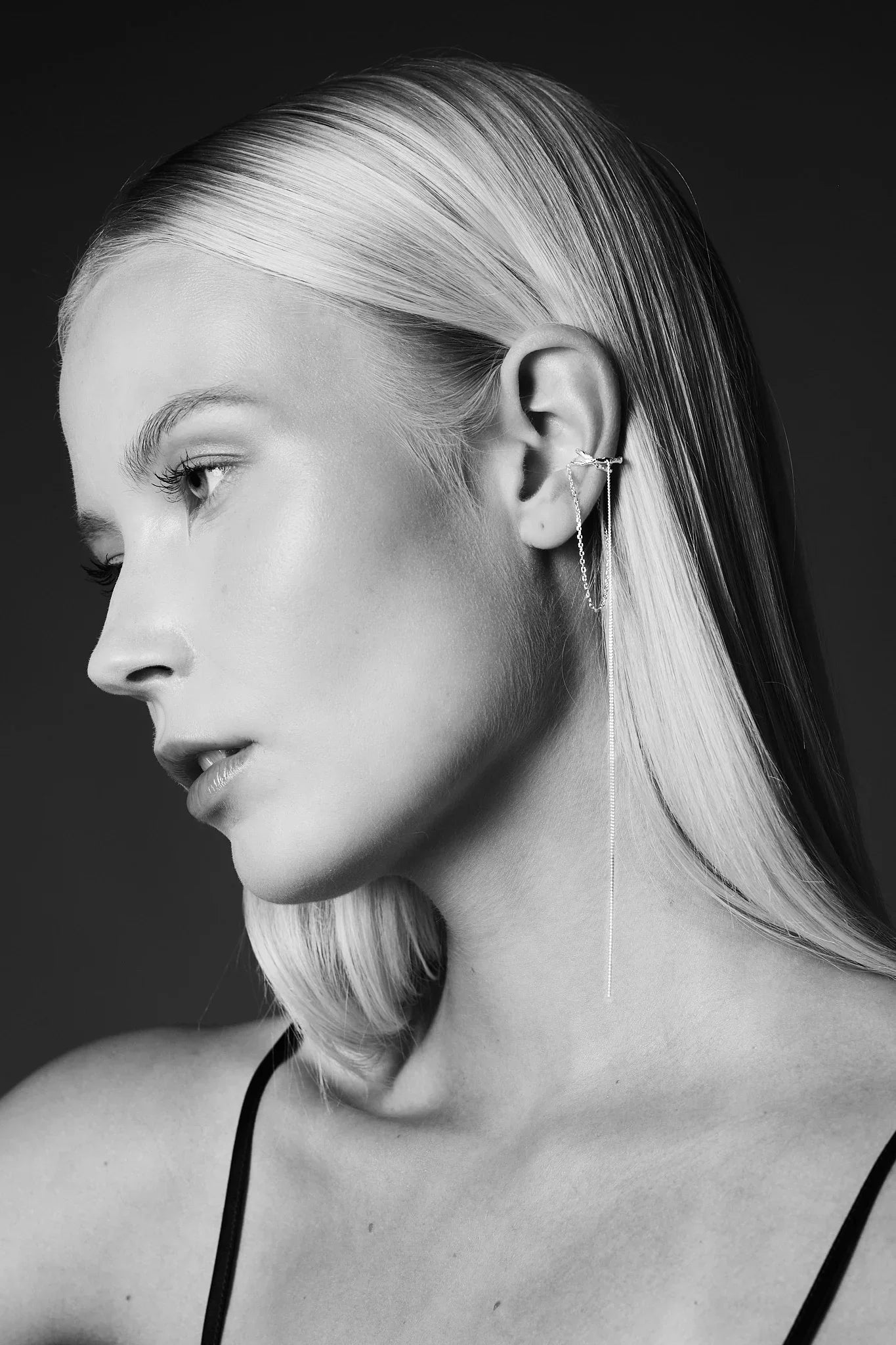 Woman wearing minimalist ear cuff with delicate chain drop earring, black and white portrait