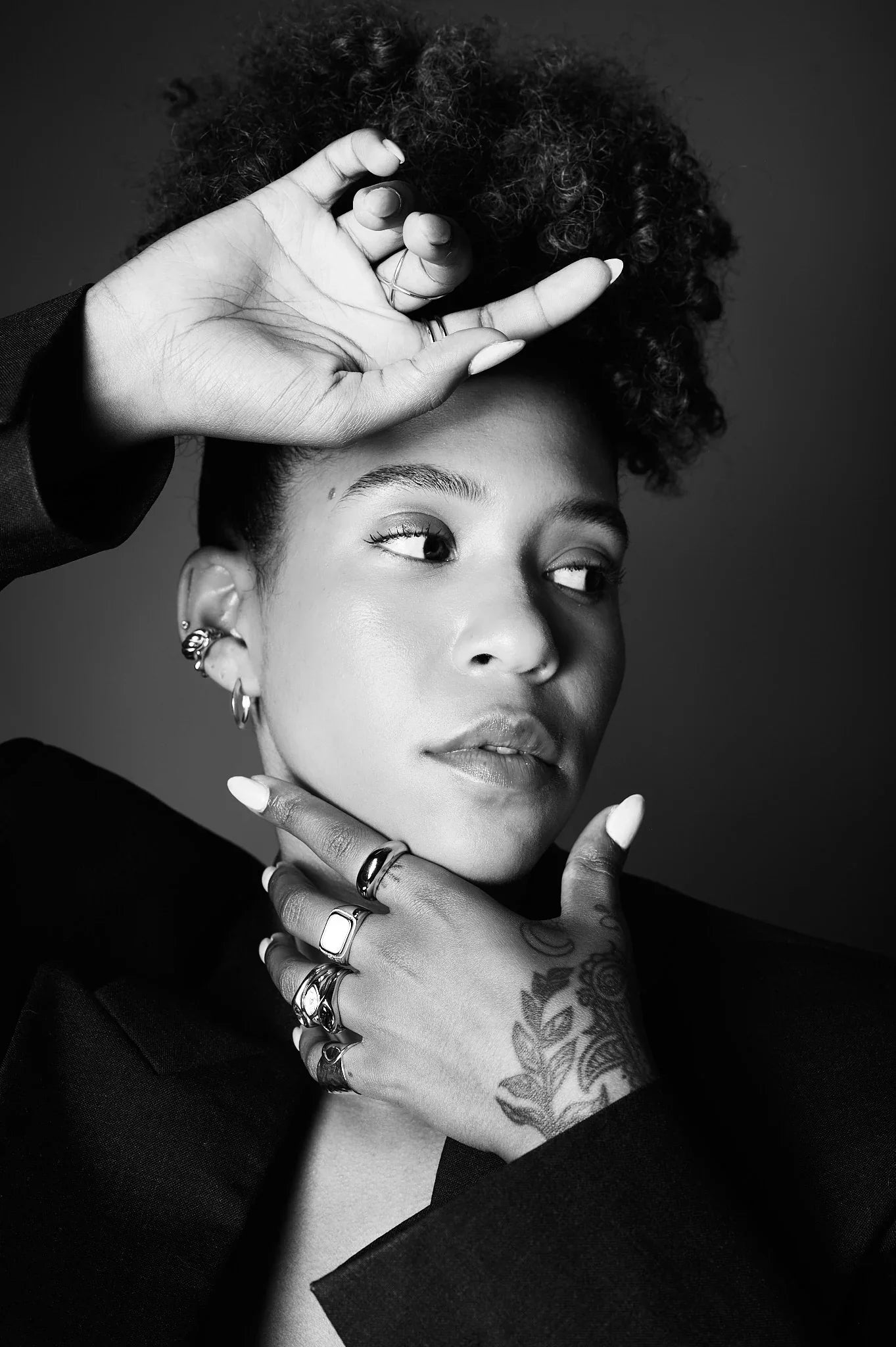 Black and white portrait of woman wearing multiple rings and earrings, showcasing jewelry