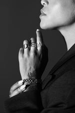 Black and white close-up of person wearing bold letter rings, watch, and suit jacket