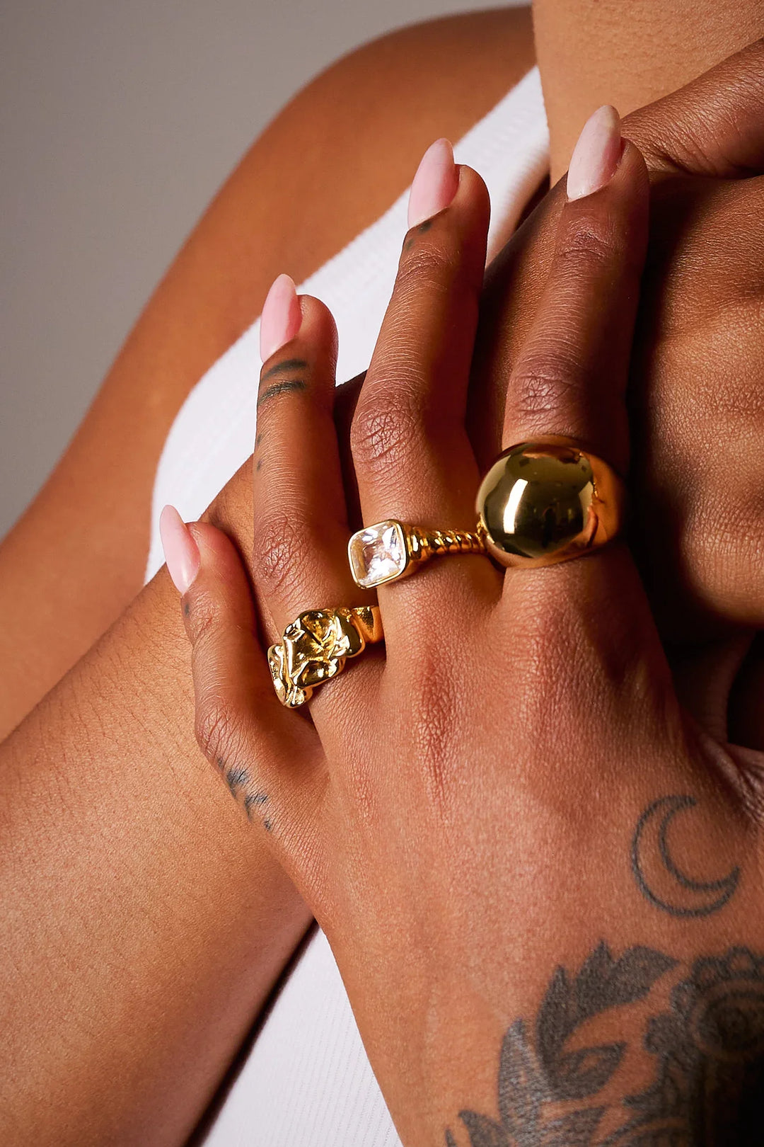 Close-up of hand with gold statement rings, gemstone ring, and minimalist nail art