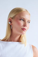Woman with straight blonde hair wearing modern silver earrings and a white sleeveless top