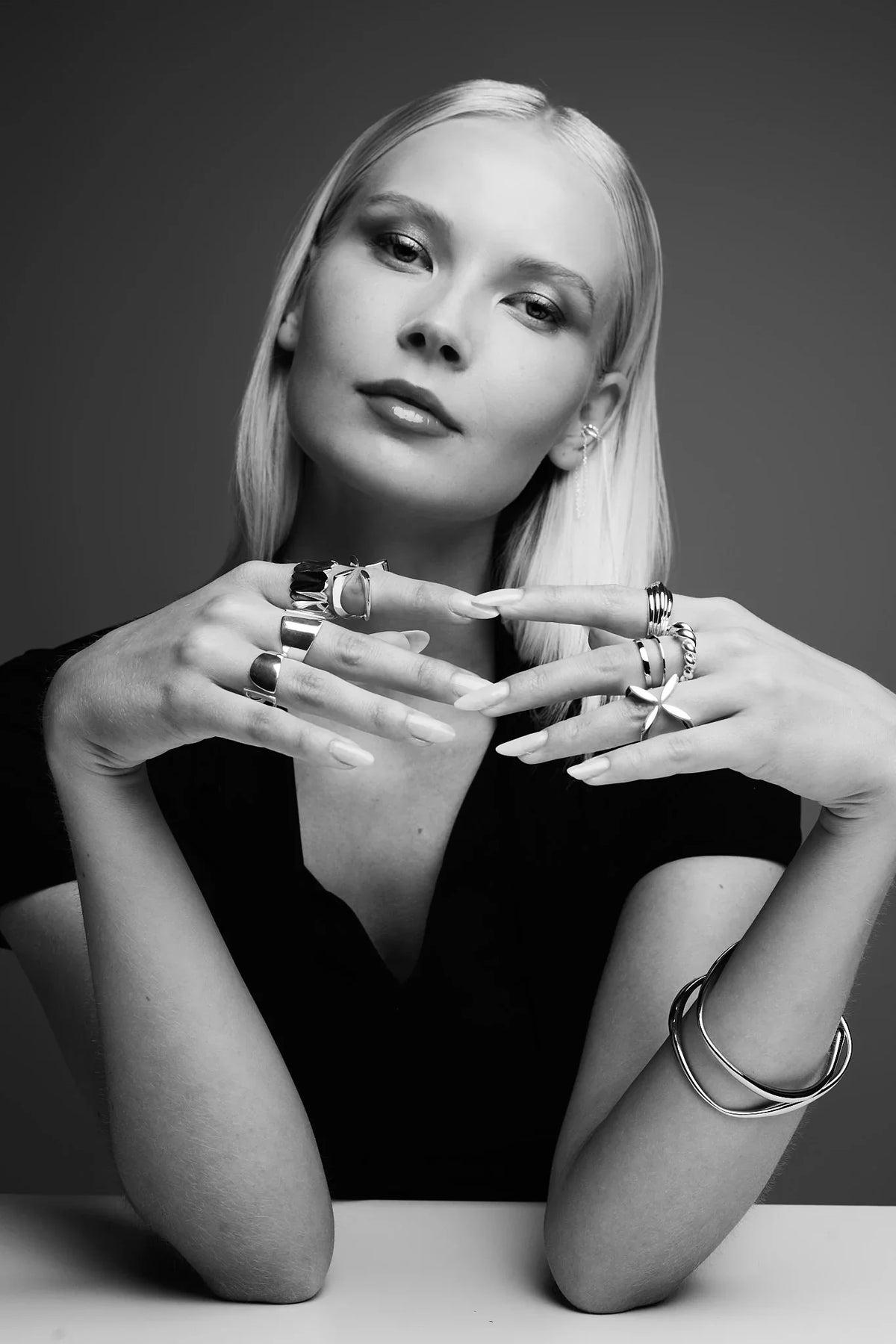 Woman modeling modern silver rings, bangles, and earrings in a black and white studio portrait.