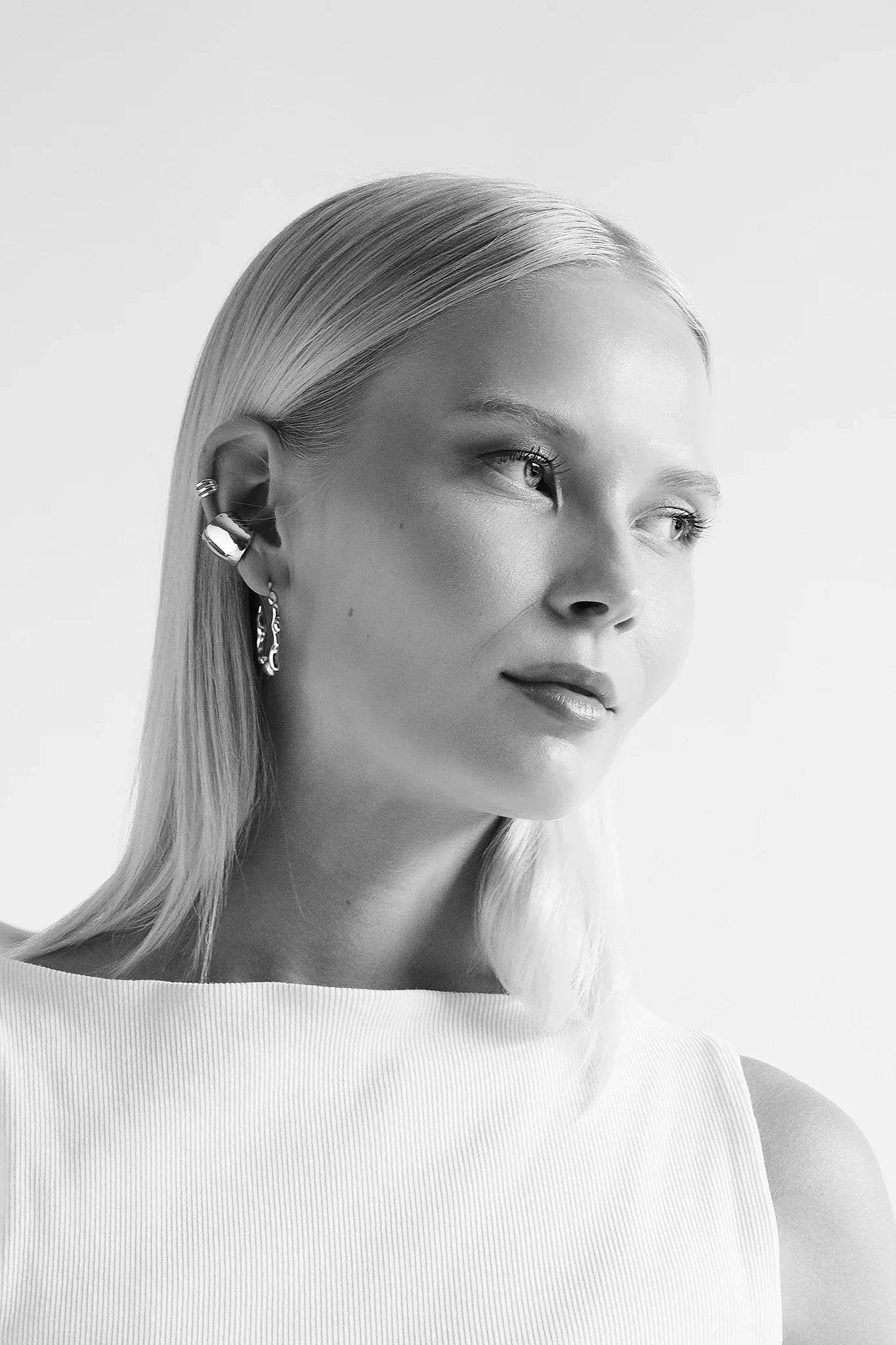 Woman with sleek blonde hair wearing modern silver earrings and a white top, minimalist style