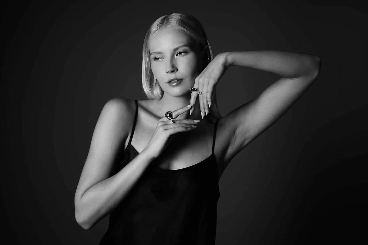 Woman in black dress showcasing bold silver rings in black and white studio portrait