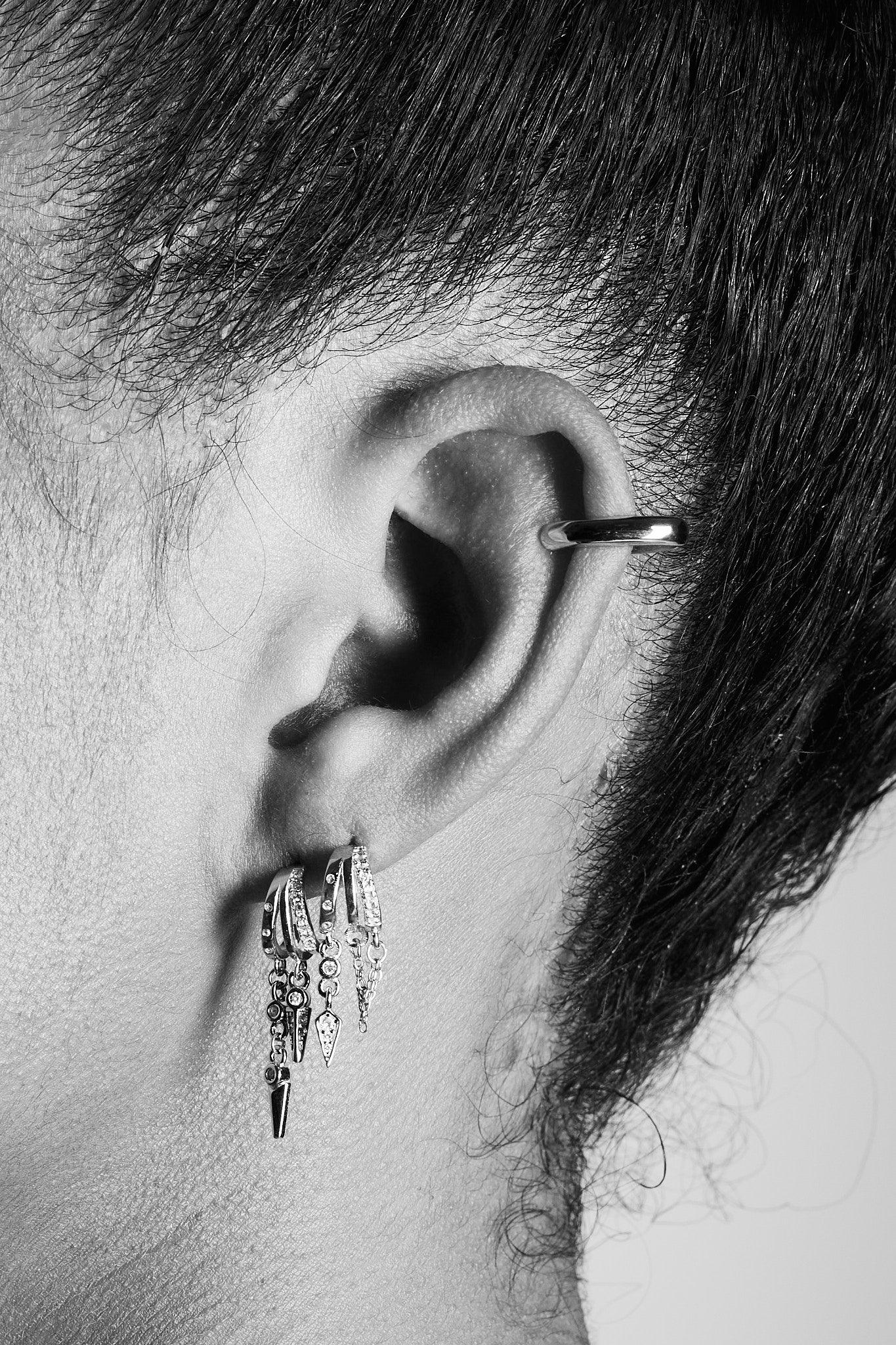 Close-up of ear wearing multiple silver hoop earrings with dangling charms