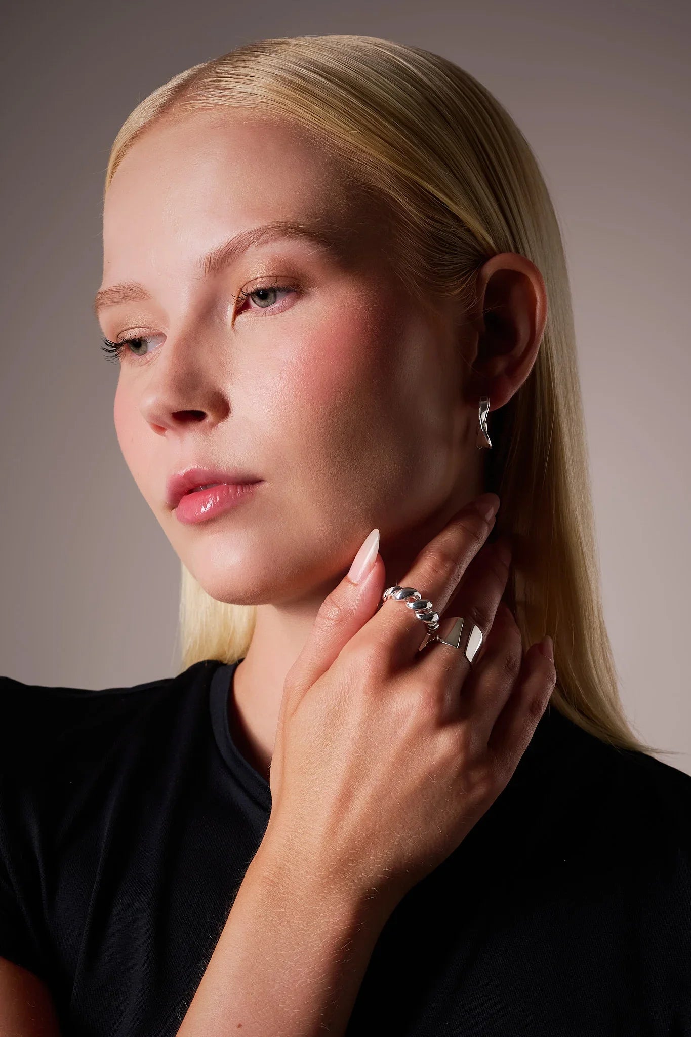 Woman wearing silver hoop earrings and chunky silver rings, close-up jewellery shot