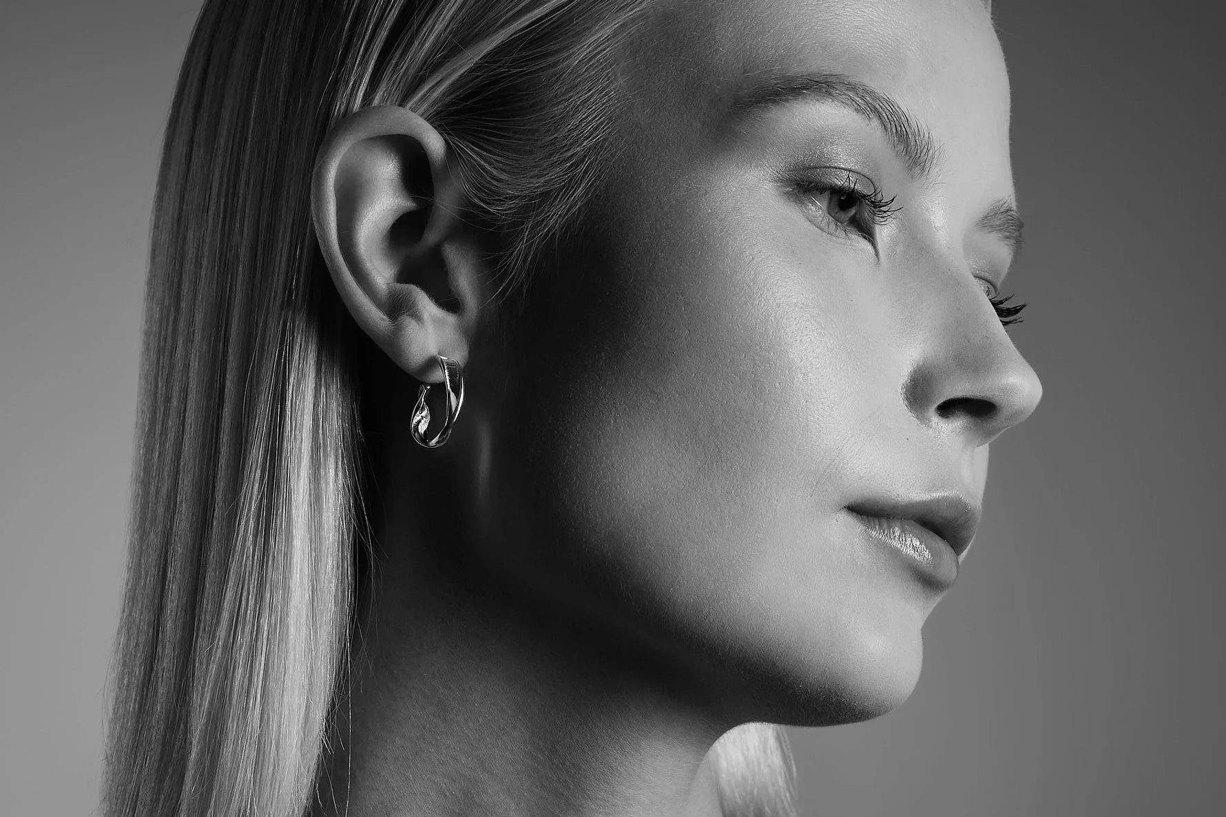 Woman wearing a twisted silver hoop earring, close-up jewelry detail