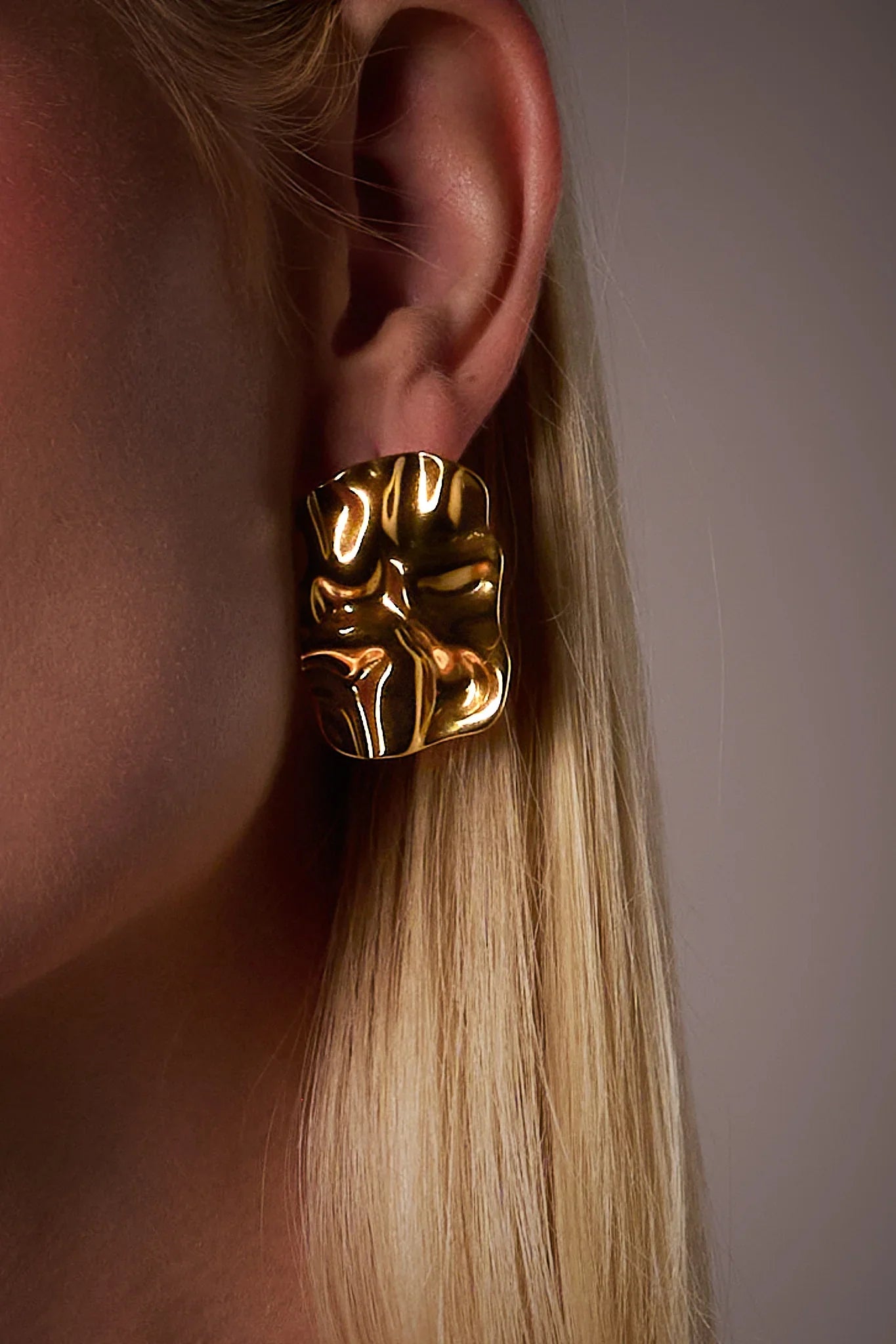 Close-up of ear wearing bold sculptural gold earring with textured, artistic finish