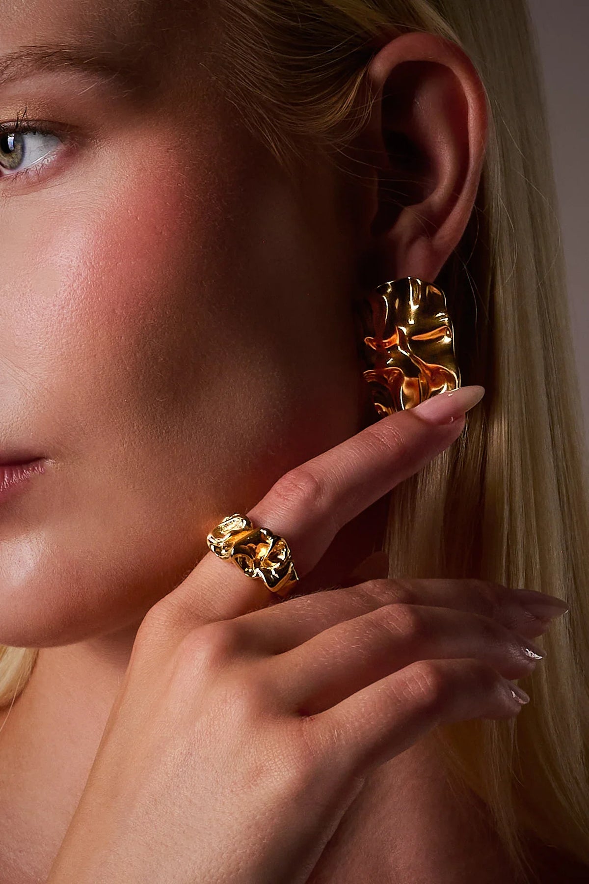 Woman wearing bold gold statement earring and matching textured gold ring