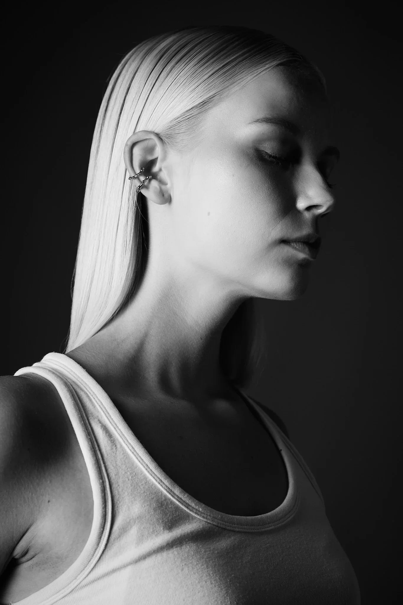 Woman with straight blonde hair wearing multiple minimalist ear cuffs, black and white close-up