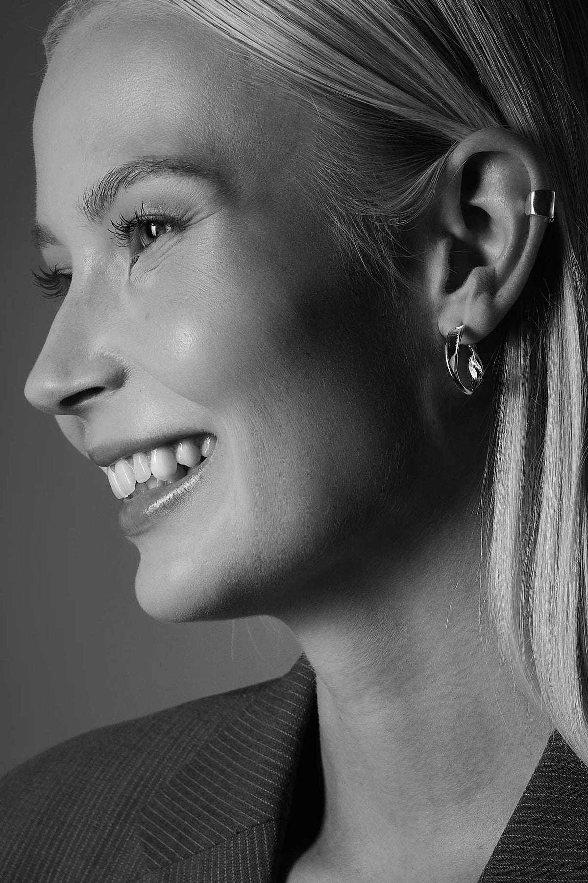 Smiling woman wearing silver hoop earrings and ear cuff, close-up jewelry portrait