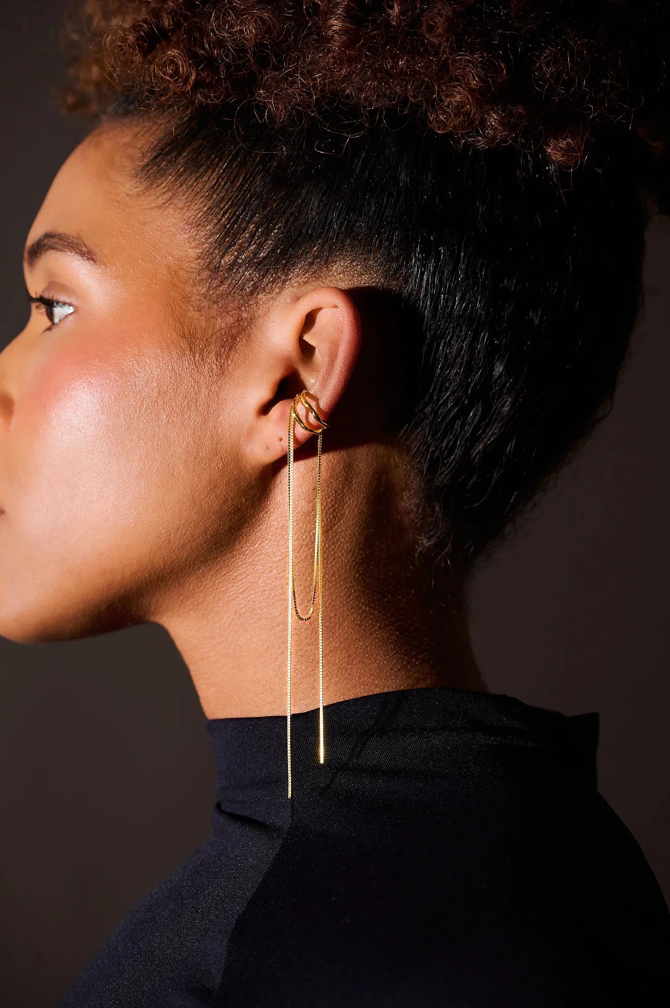 Side view of woman wearing long gold chain earrings and gold ear cuffs