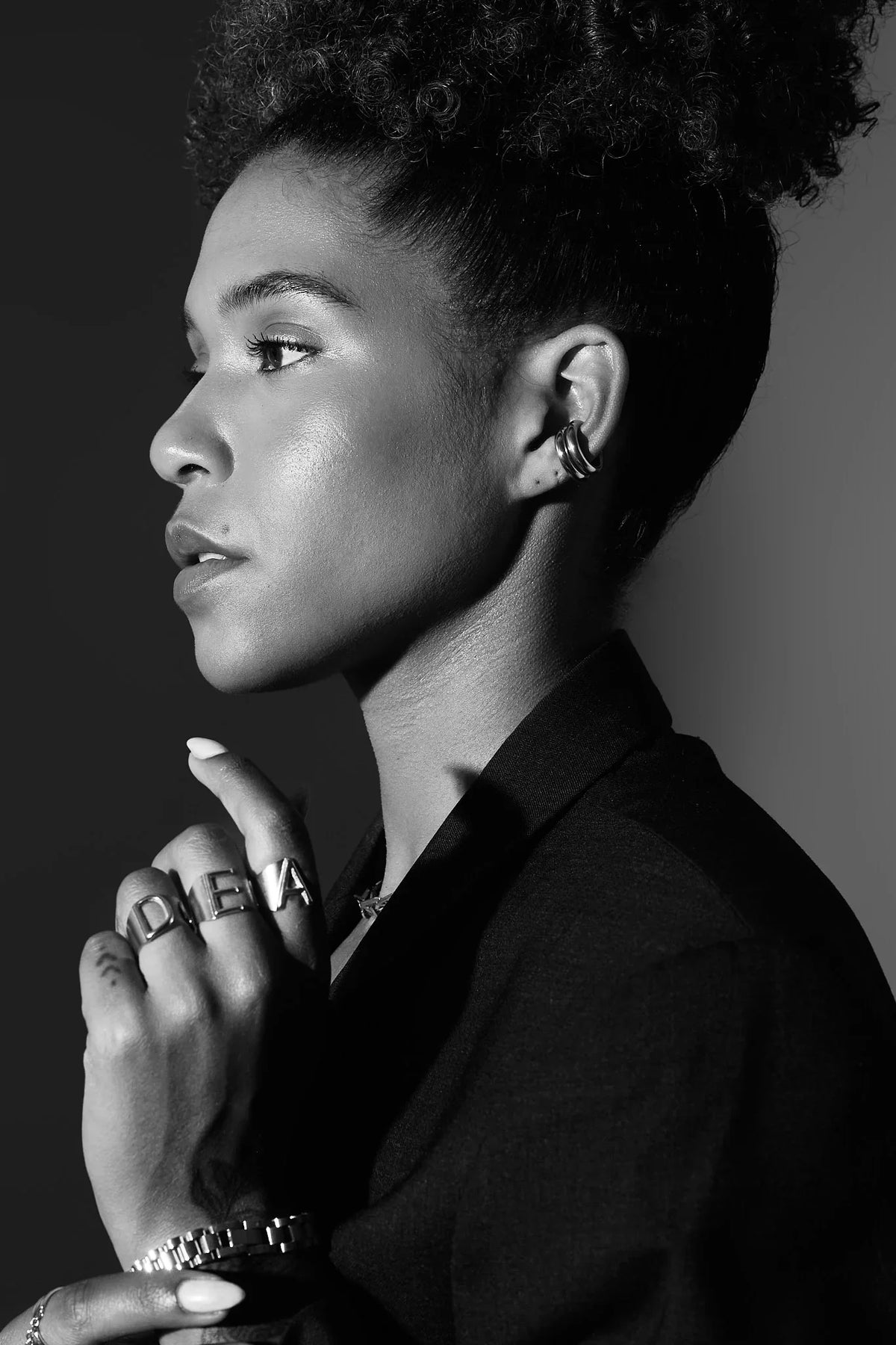 Woman wearing bold letter rings, chunky hoop earrings, and a watch in black and white portrait