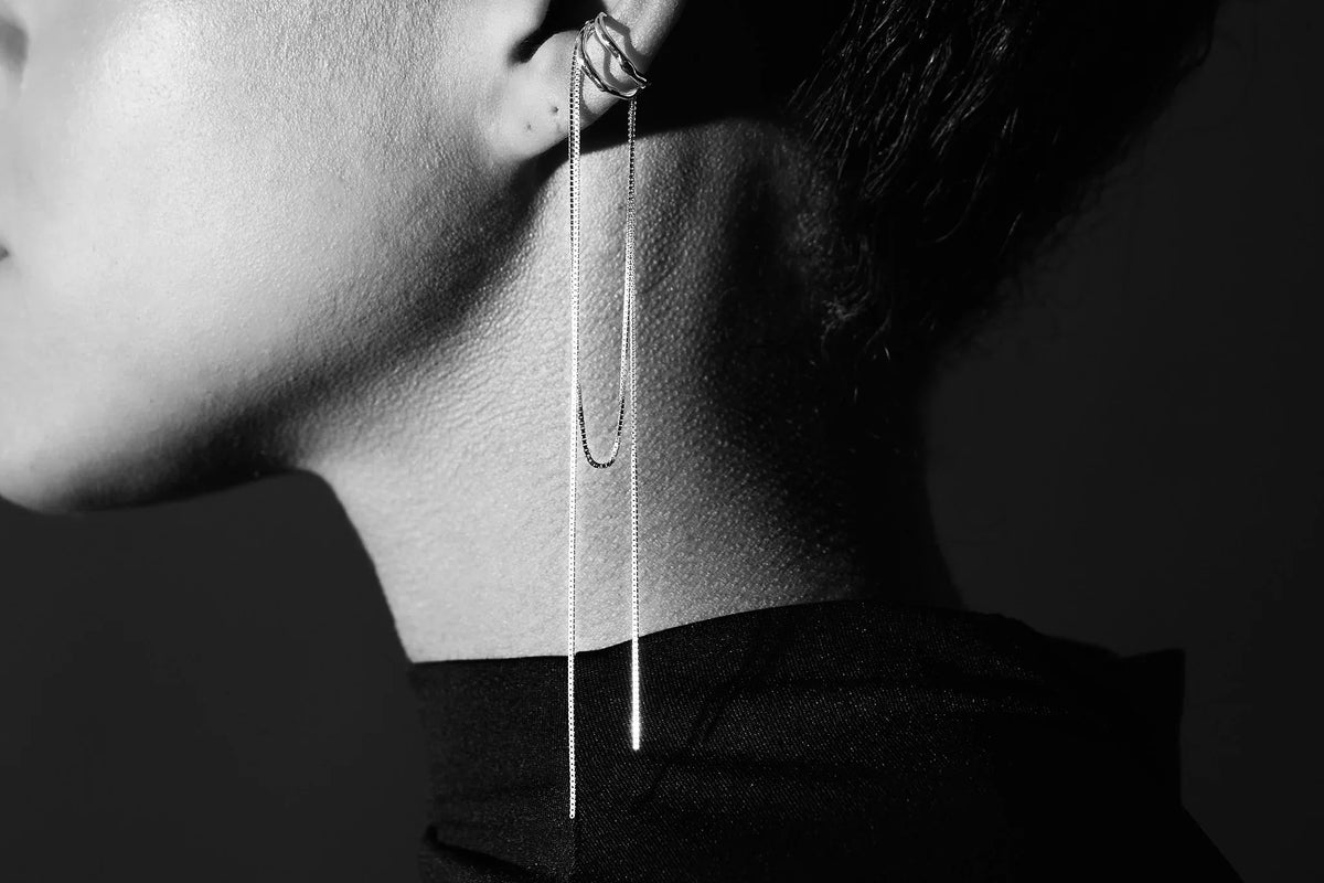 Minimalist silver ear cuff and long chain earring on model in black and white