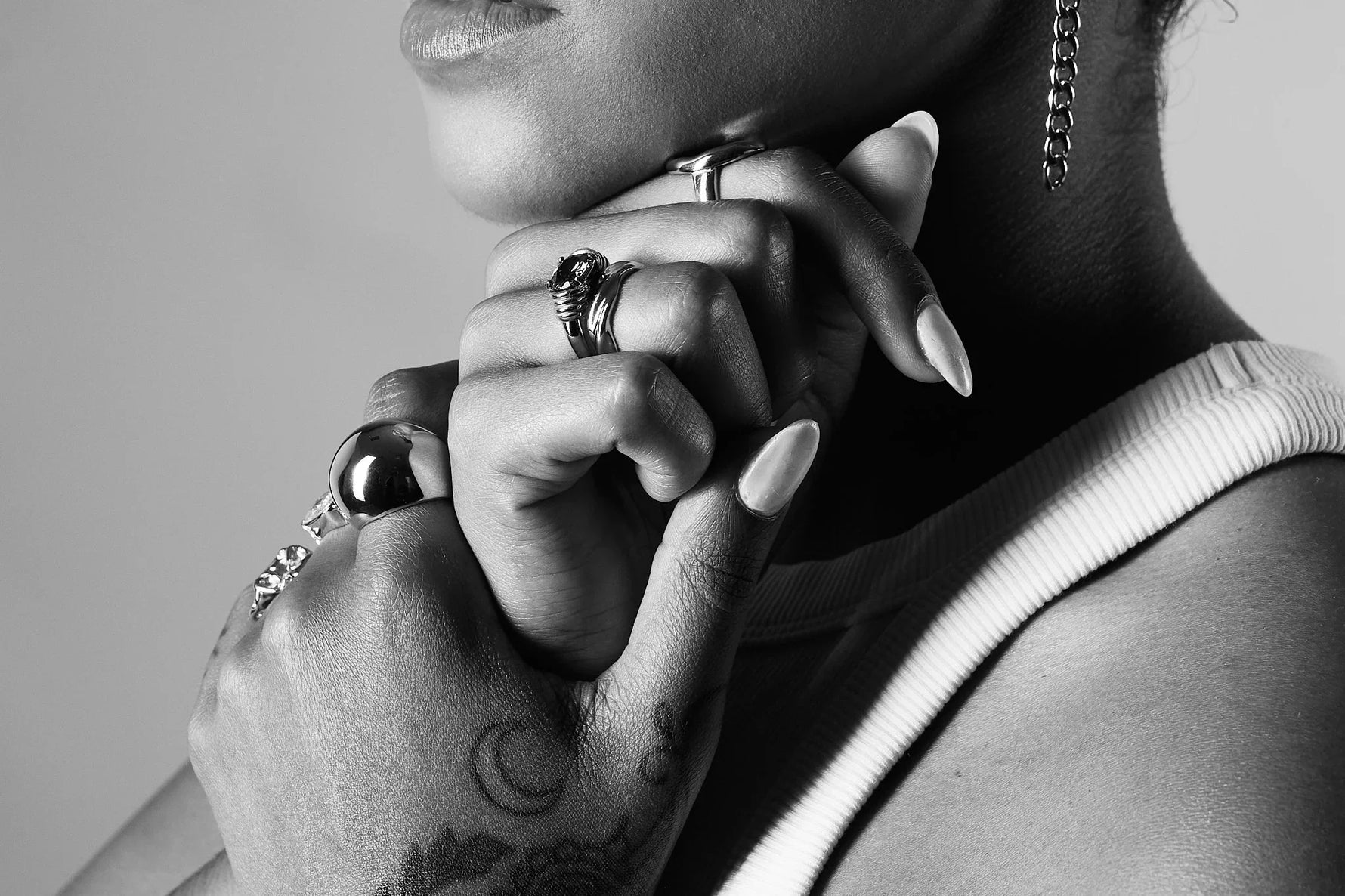 Close-up of woman wearing silver rings and chain earring with tattooed hand