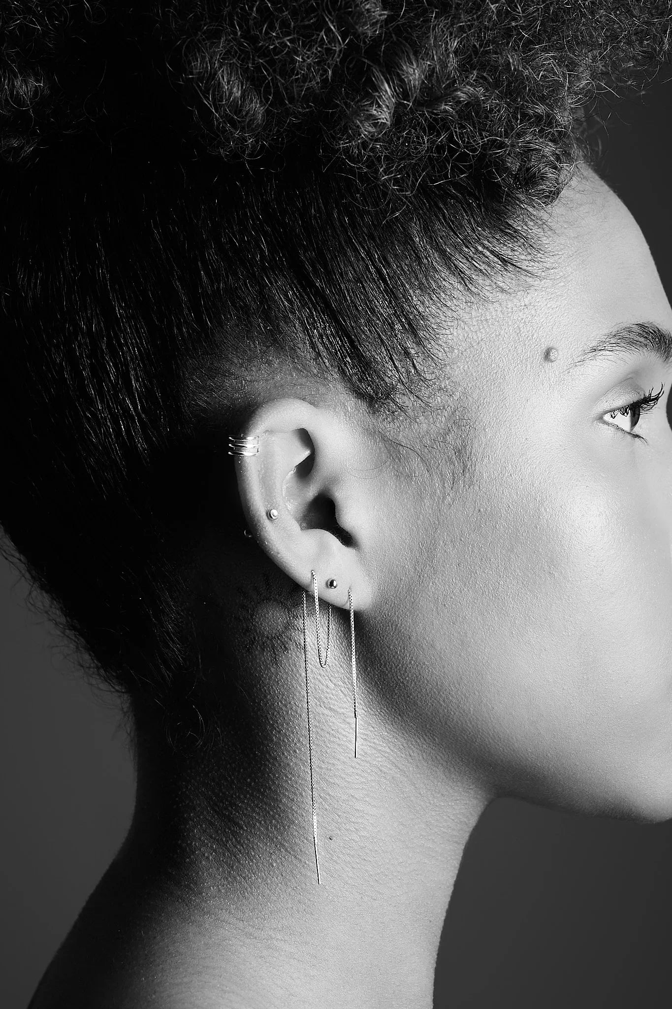Close-up of woman's ear with multiple silver earrings and ear cuff, modern jewellery style