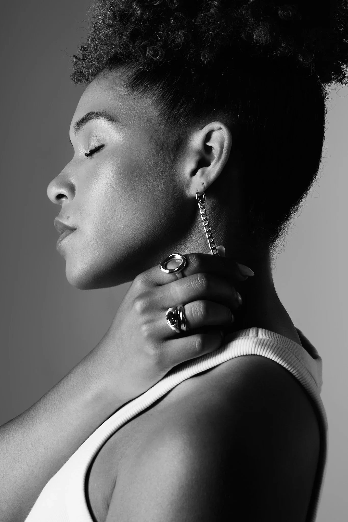 Woman wearing modern silver ring and chain drop earring, side profile, black and white