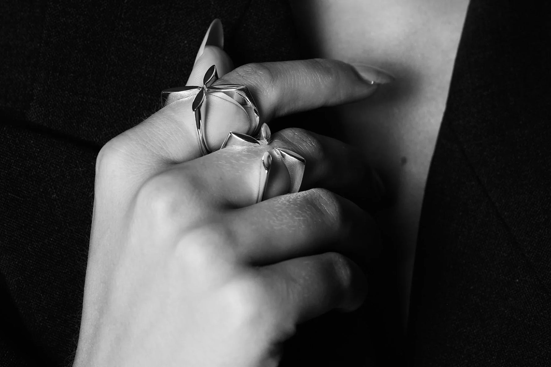 Close-up of hand wearing sculptural silver rings with leaf design, black background