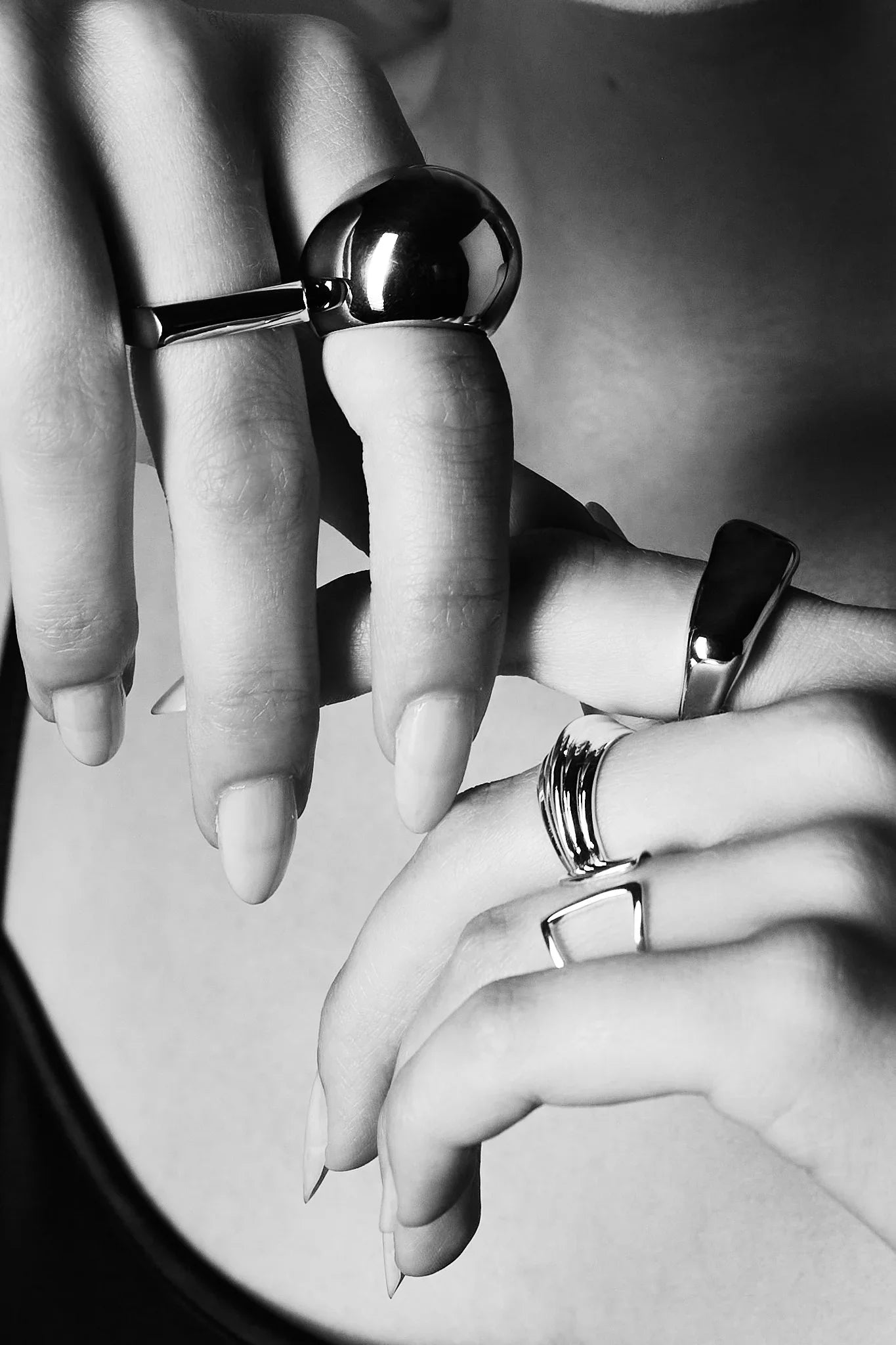 Close-up of hands wearing modern, sculptural silver rings on multiple fingers