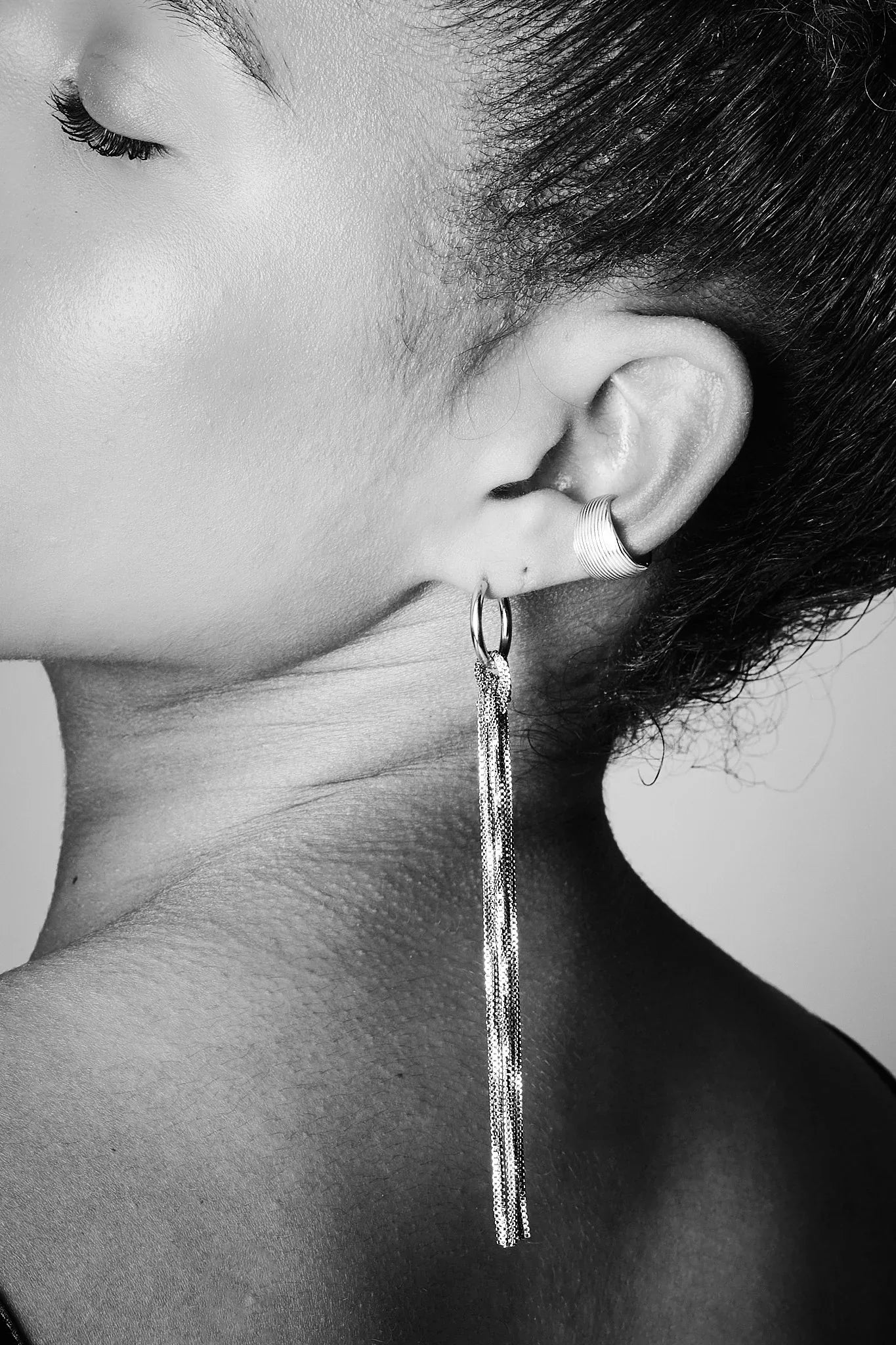 Woman wearing long silver chain drop earring and ear cuff, close-up
