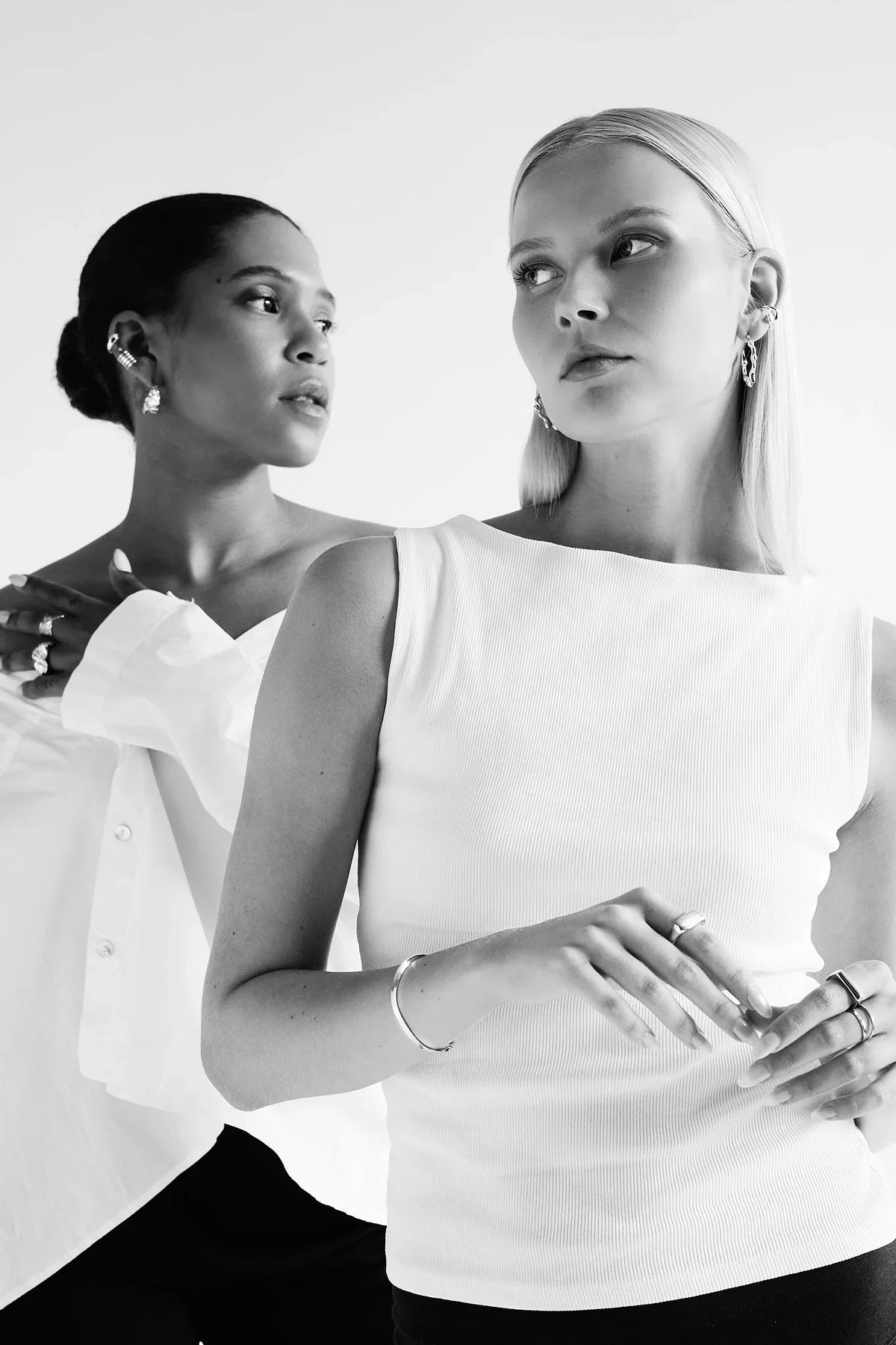 Two women modeling modern silver earrings, rings, and bracelets in a minimalist setting