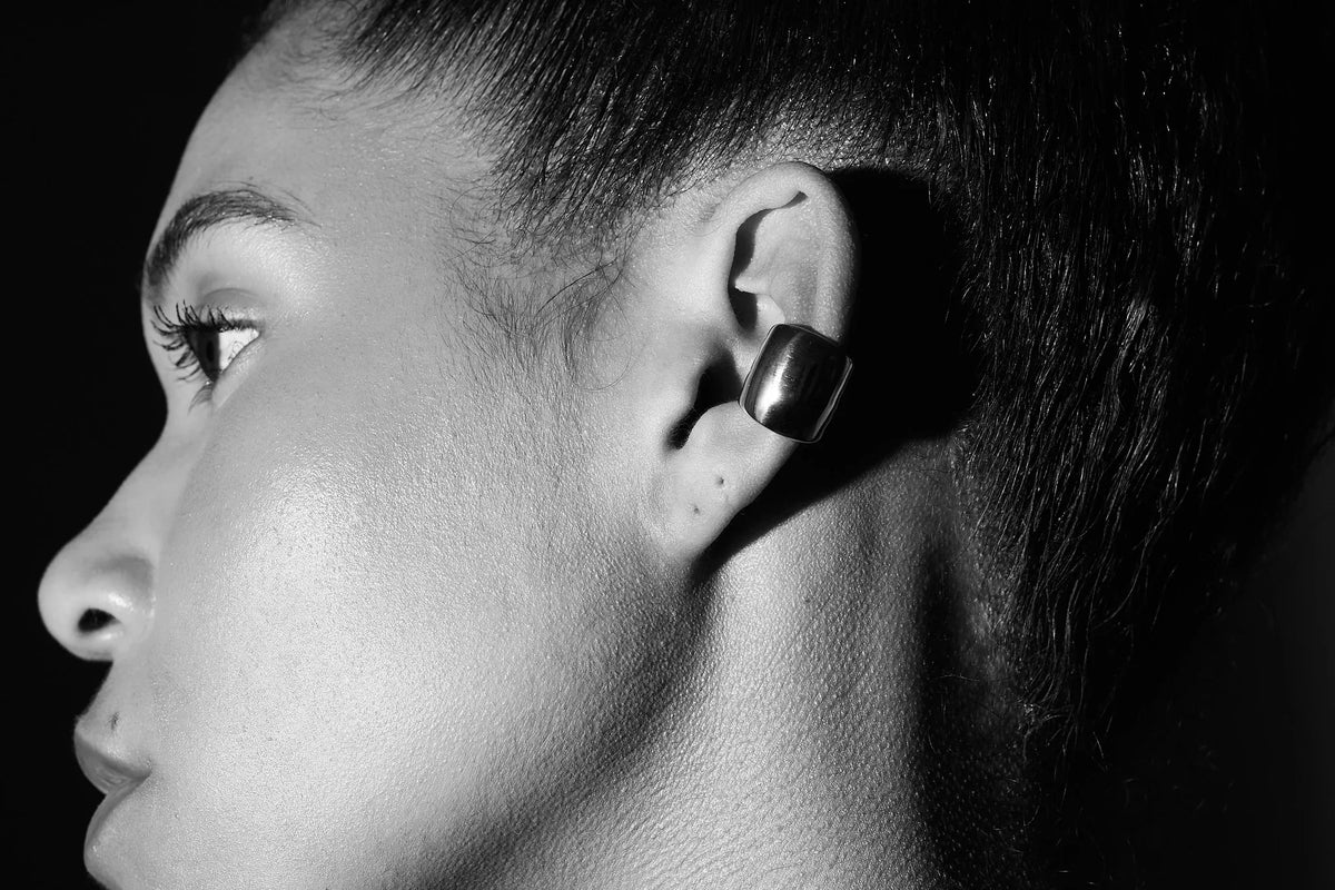 Close-up of woman wearing chunky silver ear cuff earring against dark background