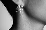 Close-up of ear wearing multiple silver hoop earrings with crystal and chain dangle charms