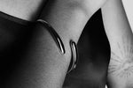 Minimalist silver cuff bracelet on wrist, close-up on dark background