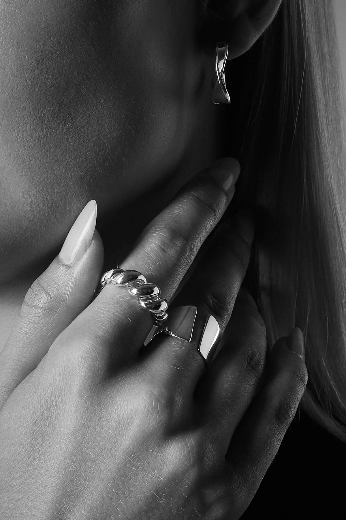 Woman wearing chunky silver rings and a twisted silver hoop earring, close-up