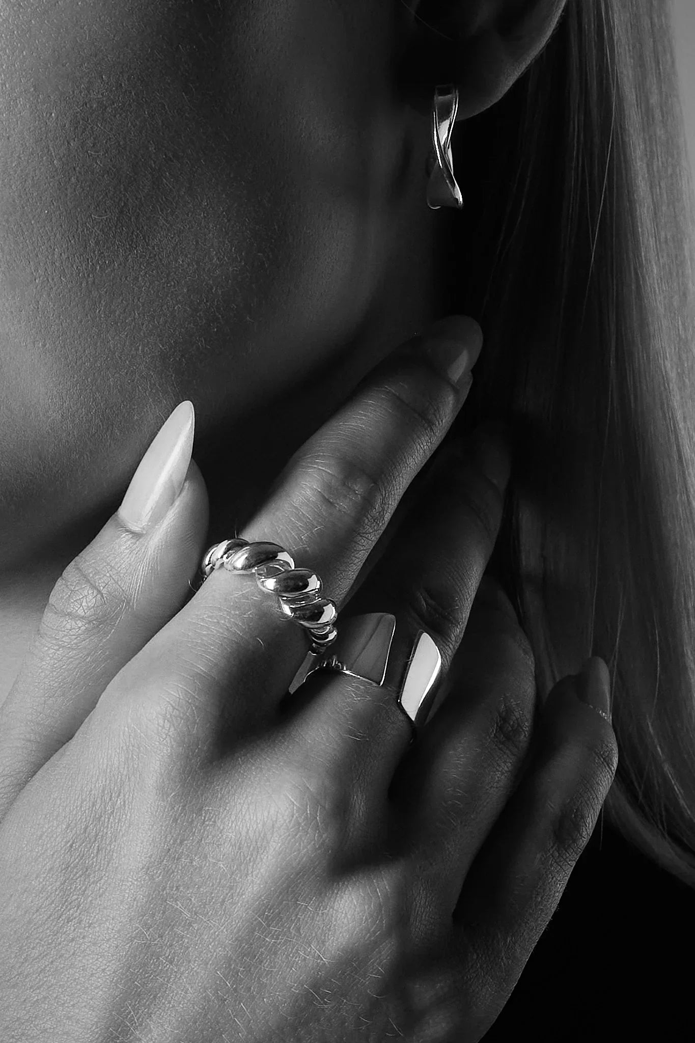Woman wearing chunky silver rings and a twisted silver hoop earring, close-up