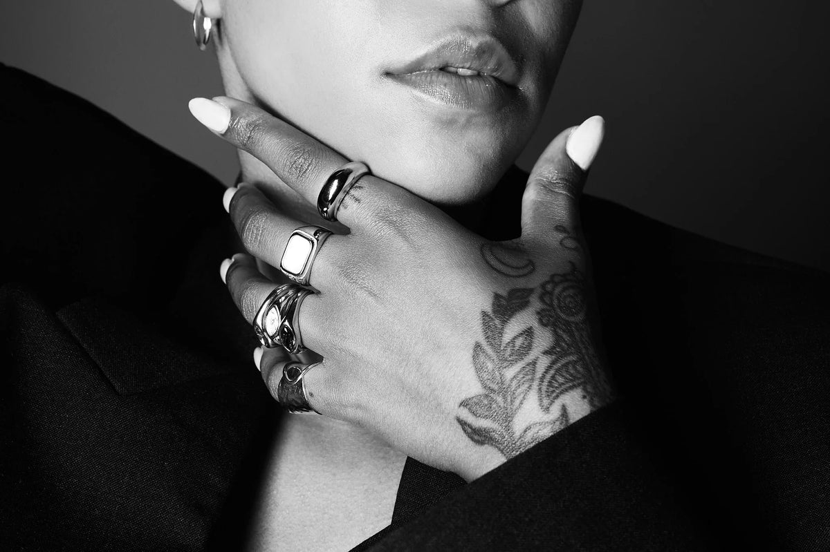Woman with tattooed hand wearing multiple silver rings, close-up on lips and fingers