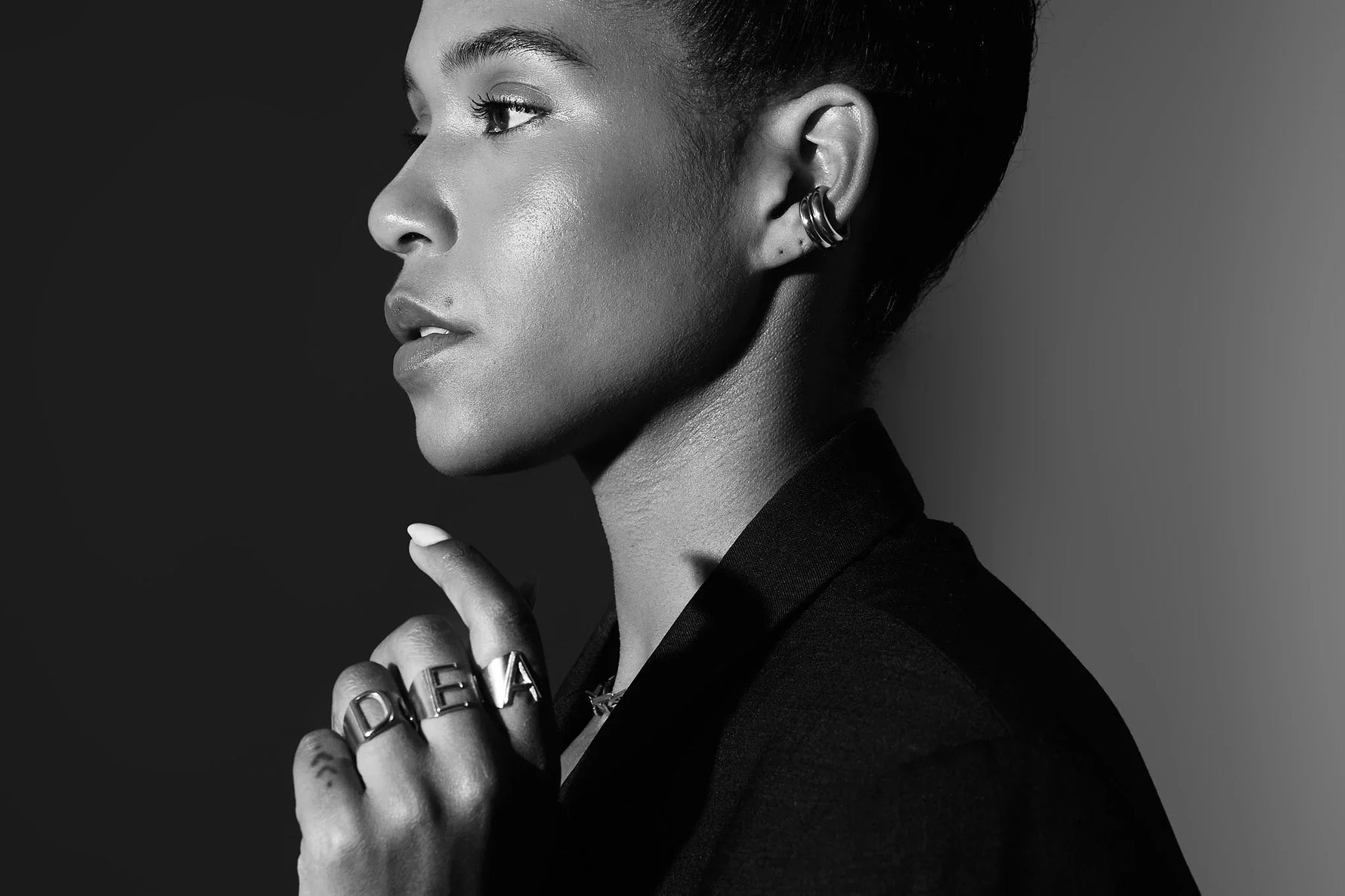 Woman wearing bold letter rings and stacked ear cuff jewellery, black and white portrait